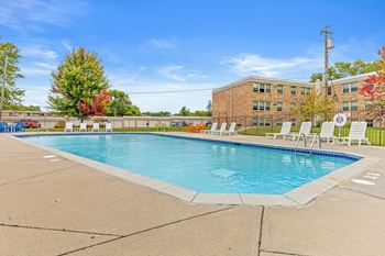 A swimming pool in front of a brick building with trees in the background.